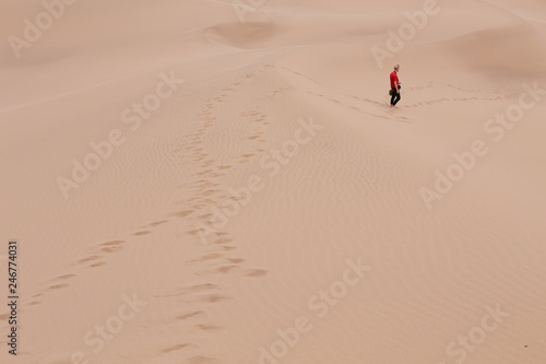 Man with red t-shirt is walking in sand dunes leaving footprint trails in beautiful orange desert sand dunes in Yazd  Iran