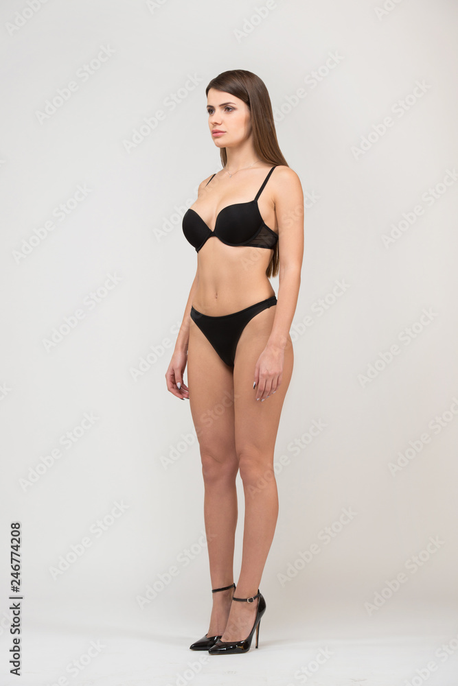 Full length portrait three-quarter of beautiful brunette women with slim figure in black bra and shorts. Model snaps in the studio on white background Full length portrait three-quarter of beautiful brunette women with slim figure in black bra and shorts. Model snaps in the studio on white background