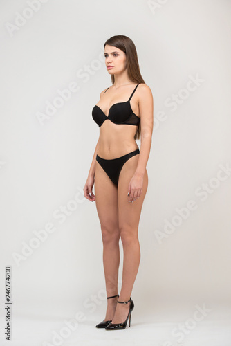 Full length portrait three-quarter of beautiful brunette women with slim figure in black bra and shorts. Model snaps in the studio on white background