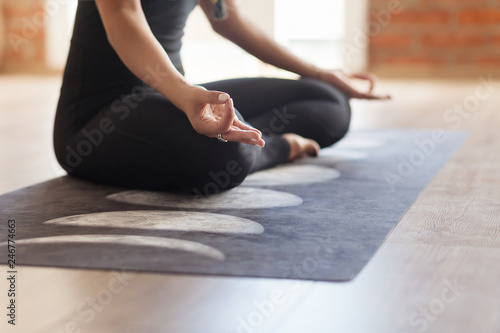 Unidentified young woman yoga instructor meditates In an empty bright room sitting in the lotus position. Concept of relaxation and exercise training