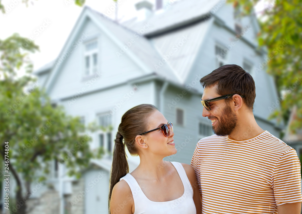 people and relationships concept - happy couple in sunglasses in summer over living house background
