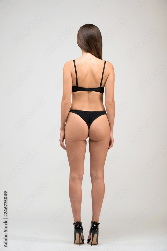 Full length portrait of beautiful brunette women with slim figure in black bra and shorts. Back view model snaps in the studio on white background Full length portrait of beautiful brunette women with slim figure in black bra and shorts. Back view model snaps in the studio on white background