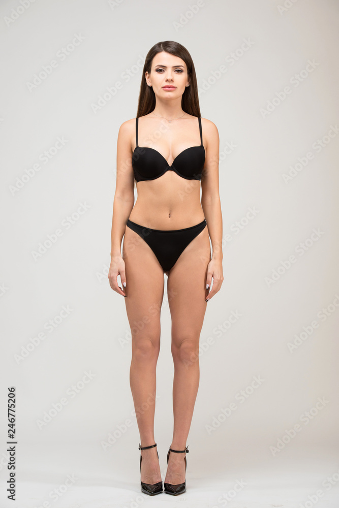 Front view full length portrait of beautiful brunette women with slim figure in black bra and shorts. Model snaps in the studio on white background Front view full length portrait of beautiful brunette women with slim figure in black bra and shorts. Model snaps in the studio on white background