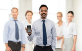 business, technology and people concept - smiling indian businessman with smartphone over colleagues on office background