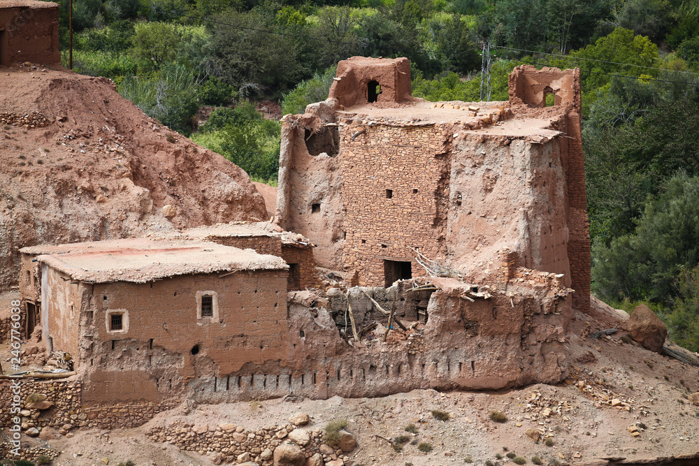 Ruins of old Berber village with mud brick architecture in the green oasis of a river valley surrounded by the arid desert landscape of the Atlas Mountains in Morocco
