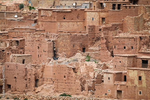 Old Berber village with mud brick architecture in the green oasis of a river valley surrounded by the arid desert landscape of the Atlas Mountains in Morocco.
