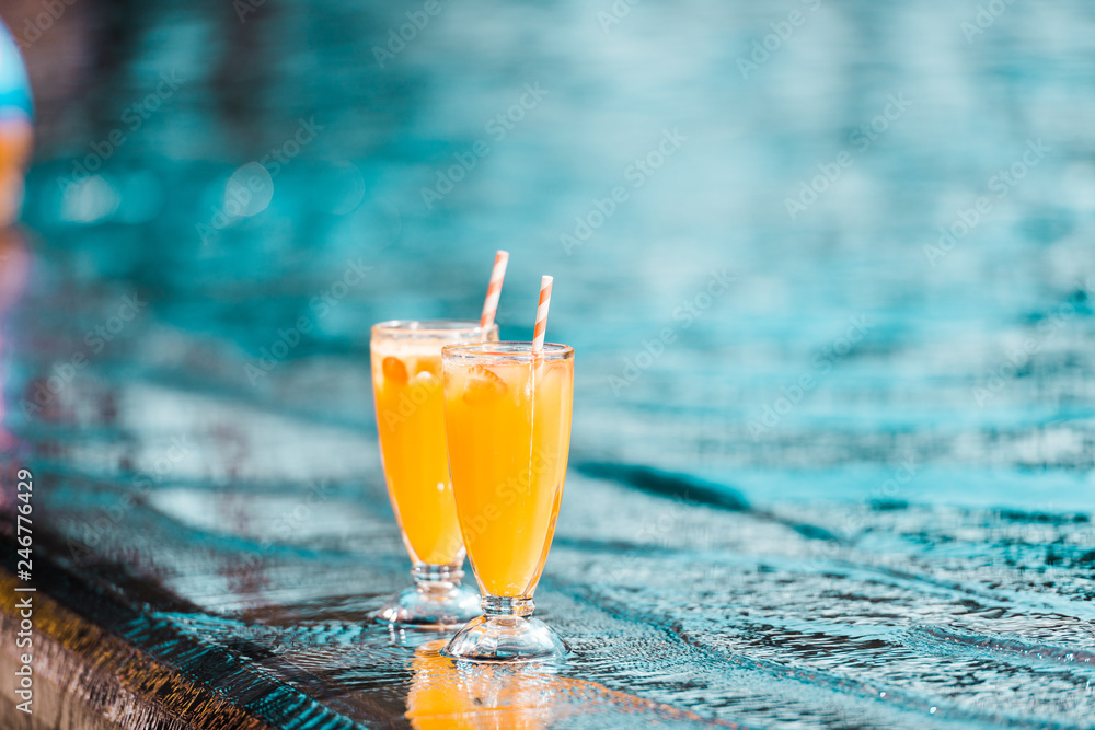 two orange cocktails glasses with straws standing at poolside two orange cocktails glasses with straws standing at poolside