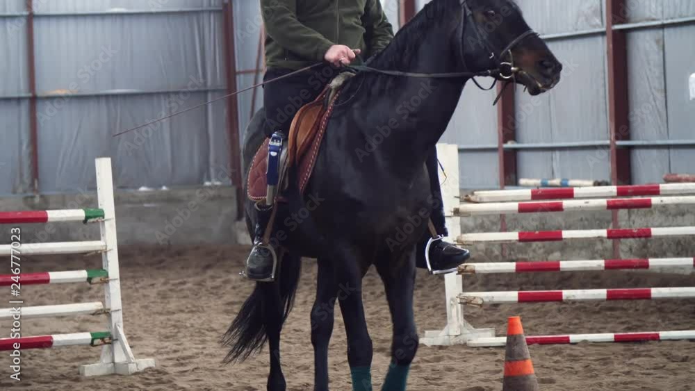 in special hangar, a young disabled man learns to ride a black, thoroughbred horse, hippotherapy. man has an artificial limb instead of his right leg. concept of rehabilitation of disabled with in special hangar, a young disabled man learns to ride a black, thoroughbred horse, hippotherapy. man has an artificial limb instead of his right leg. concept of rehabilitation of disabled with