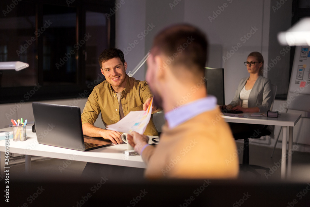 business, deadline and people concept - man giving papers to colleague at night office