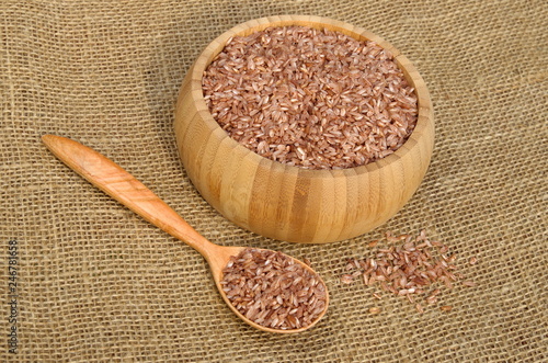 Uzbek devzira, the red rice in a bamboo bowl and in wooden spoon on burlap photo