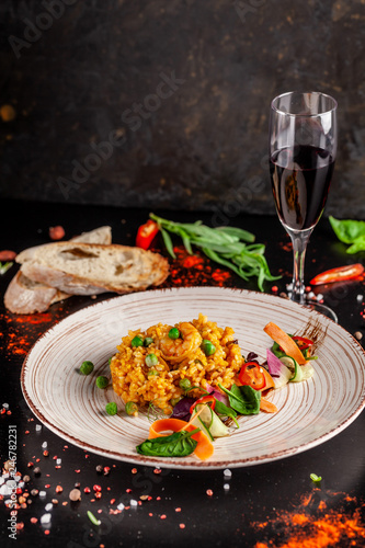 Concept of Spanish cuisine. Paella with seafood and shrimps, with green peas in a clay plate. A glass of cool wine is on the table. background image, copy space