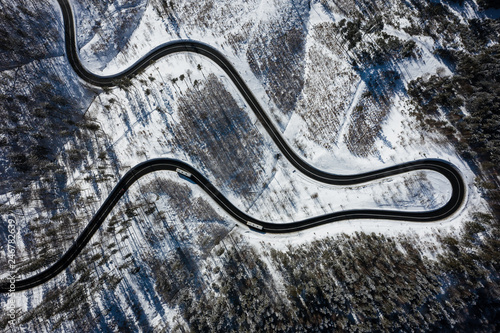 Curvy windy road in snow covered forest, top down aerial view. Winter landscape.