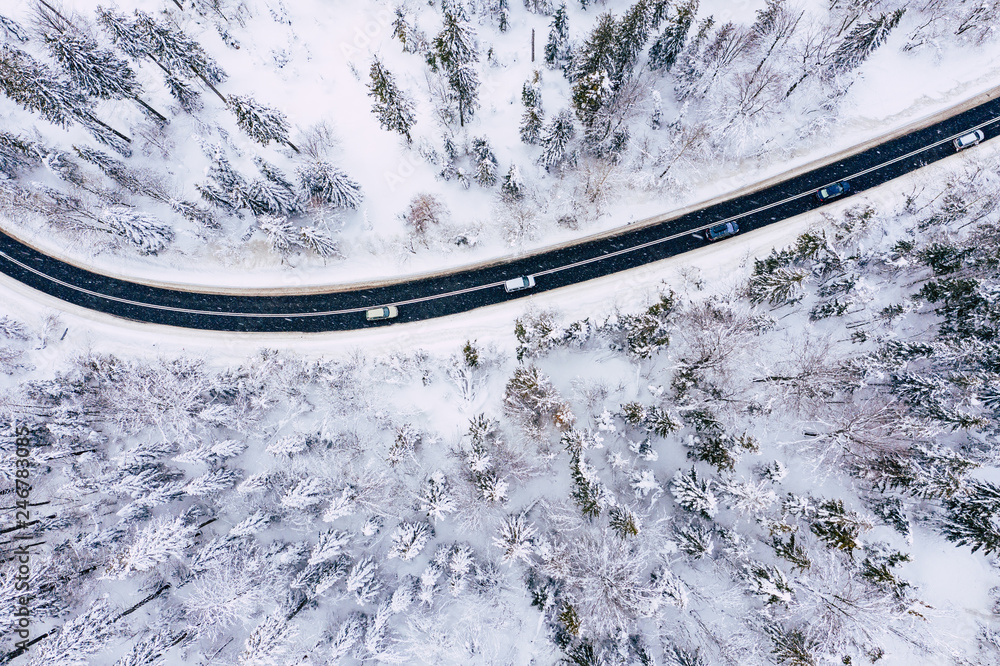 Curvy windy road in snow covered forest, top down aerial view. Winter landscape.
