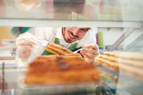 Worker in pastry shop taking piece of cake