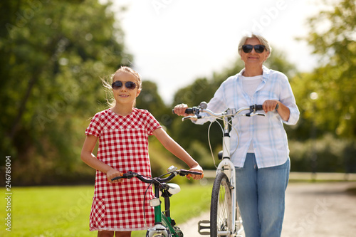 family, leisure and people concept - happy grandmother and granddaughter with bicycles at summer park