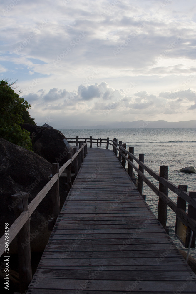 Obraz premium Wooden board bridge around cliff cape with cloudy sky above the sea