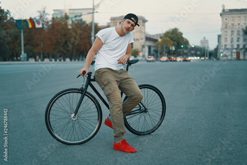 Portrait of young man walking with thoughtfully classic bicycle on city streets