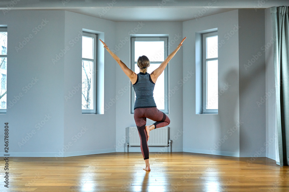 Young sporty woman practicing yoga, working out, wearing sportswear, pants and top, indoor close up, yoga studio. Rear view Young sporty woman practicing yoga, working out, wearing sportswear, pants and top, indoor close up, yoga studio. Rear view
