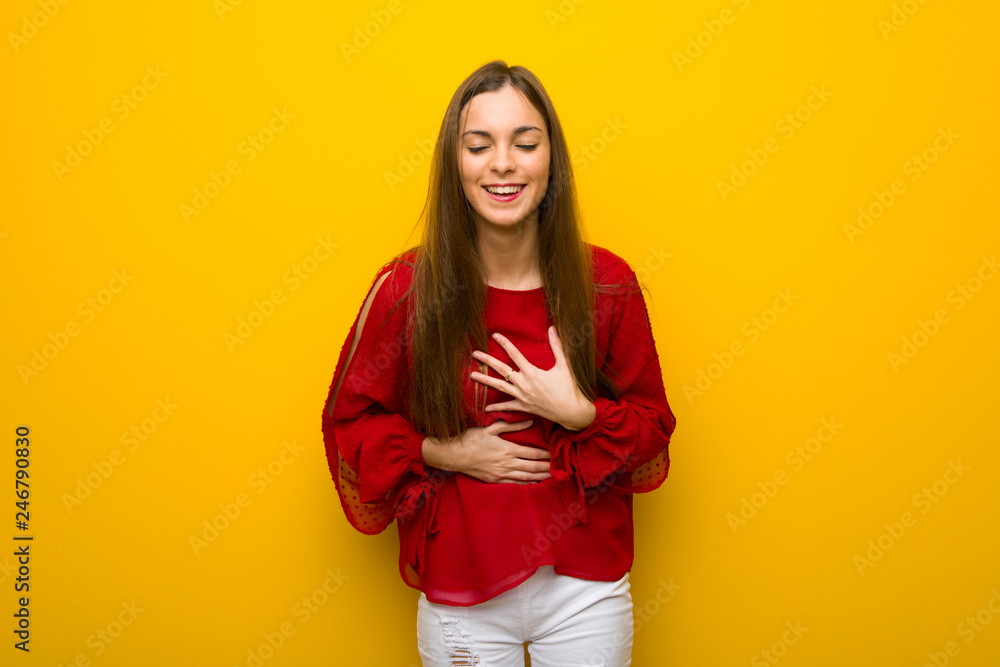 Young girl with red dress over yellow wall smiling a lot while putting hands on chest Young girl with red dress over yellow wall smiling a lot while putting hands on chest