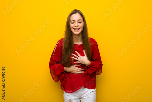 Young girl with red dress over yellow wall smiling a lot while putting hands on chest © luismolinero