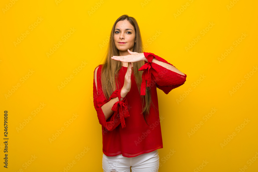 Young girl with red dress over yellow wall making stop gesture with her hand to stop an act Young girl with red dress over yellow wall making stop gesture with her hand to stop an act