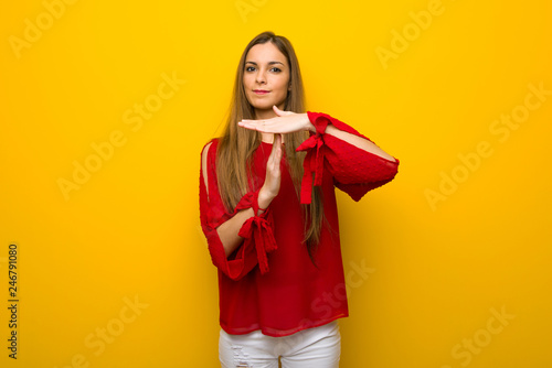 Young girl with red dress over yellow wall making stop gesture with her hand to stop an act