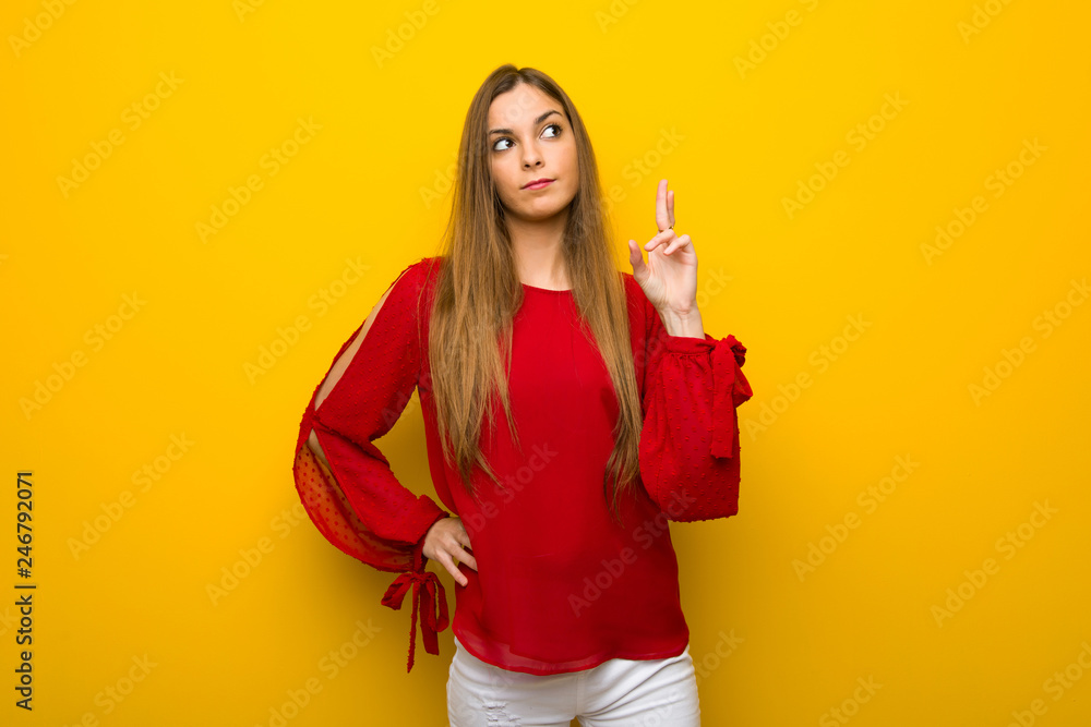 Young girl with red dress over yellow wall with fingers crossing and wishing the best Young girl with red dress over yellow wall with fingers crossing and wishing the best