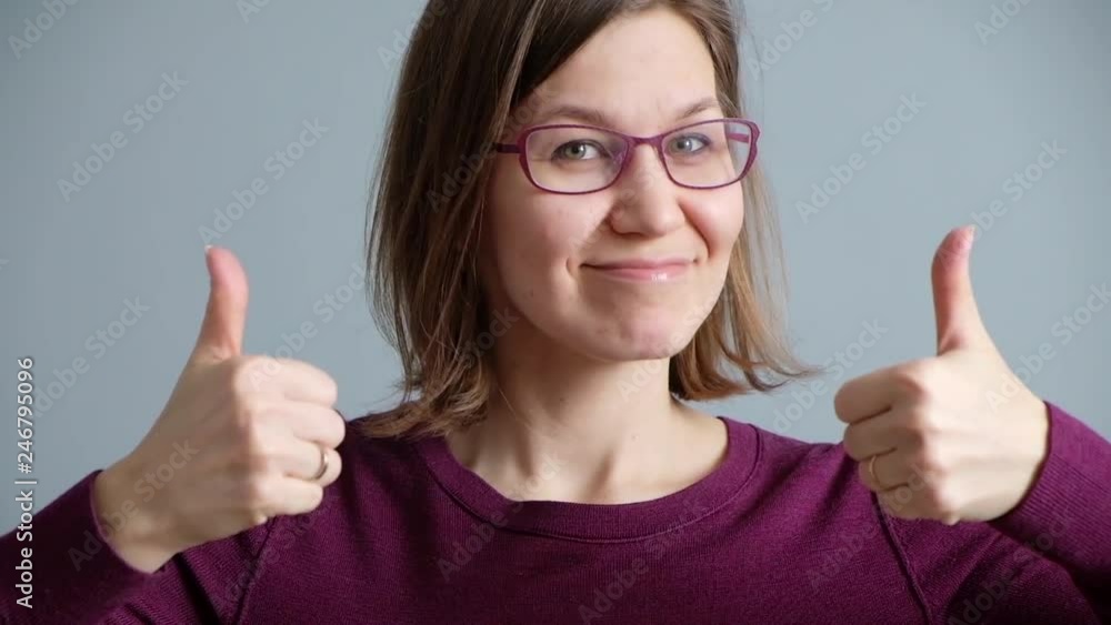 Smiling happy woman showing thumbs up and looking at the camera over gray background Smiling happy woman showing thumbs up and looking at the camera over gray background