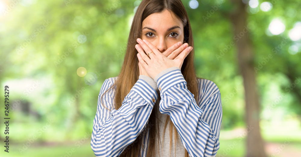 Young girl with striped shirt covering mouth with hands for saying something inappropriate at outdoors Young girl with striped shirt covering mouth with hands for saying something inappropriate at outdoors