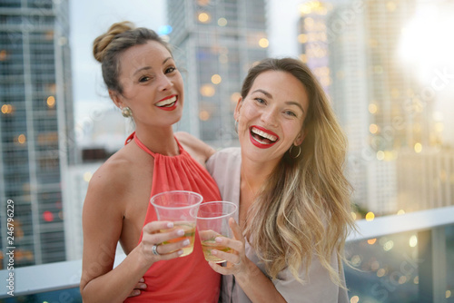 Two gorgeous friends having fun on rooftop bar in city at night fall