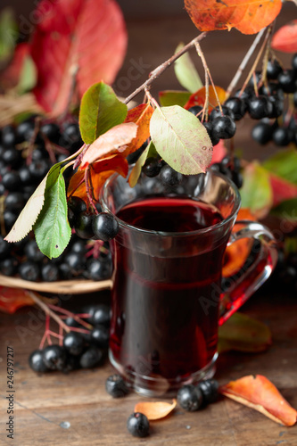 Fresh juice of ripe black chokeberry in glass and berries with leaves.