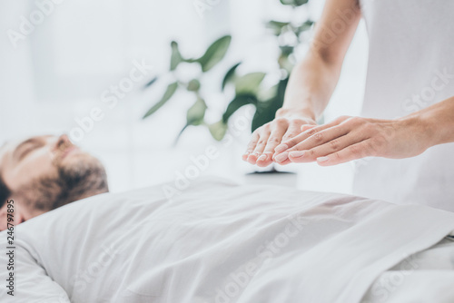 cropped shot of bearded man lying and receiving reiki treatment on stomach photo