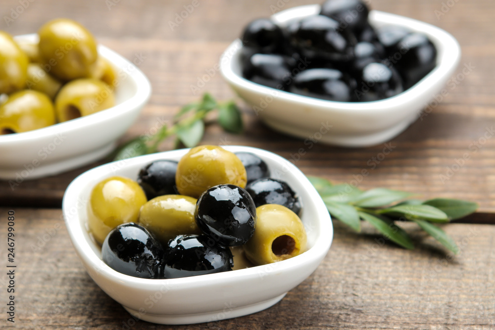Green and black olives with leaves in a white bowl on a brown wooden table. close-up Green and black olives with leaves in a white bowl on a brown wooden table. close-up