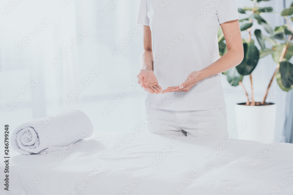 mid section of reiki healer standing near white massage table