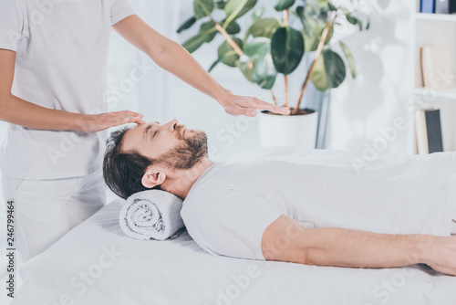 cropped shot of reiki healer doing treatment session to calm bearded man with closed eyes