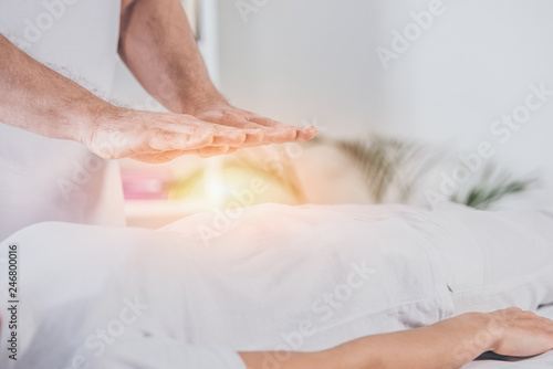 cropped shot of male healer doing reiki treatment session to woman