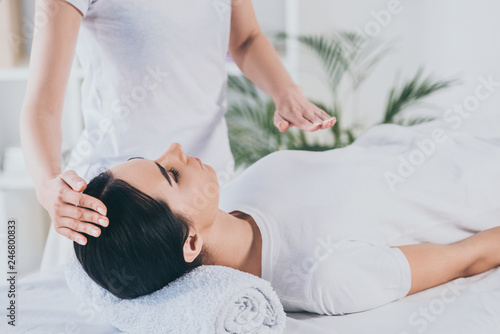 cropped shot of peaceful young woman receiving reiki healing treatment on head and chest