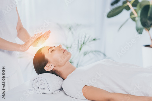 Obraz na plátně peaceful young woman with closed eyes receiving reiki treatment on head