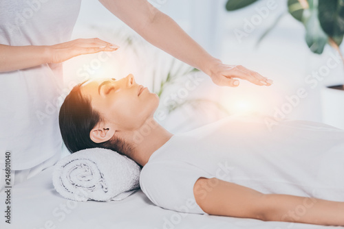 cropped shot of reiki healer doing therapy session to calm young woman with closed eyes photo