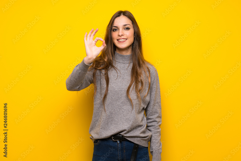 Young woman over yellow wall showing an ok sign with fingers Young woman over yellow wall showing an ok sign with fingers