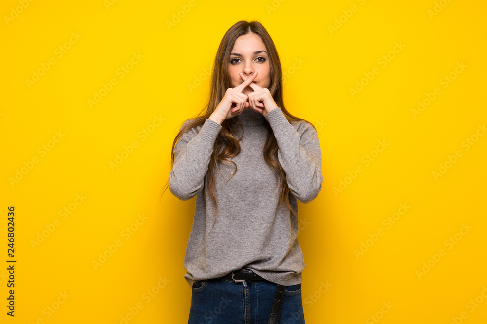 Young woman over yellow wall showing a sign of silence gesture Young woman over yellow wall showing a sign of silence gesture