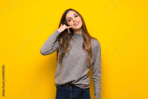 Young woman over yellow wall making phone gesture. Call me back sign © luismolinero