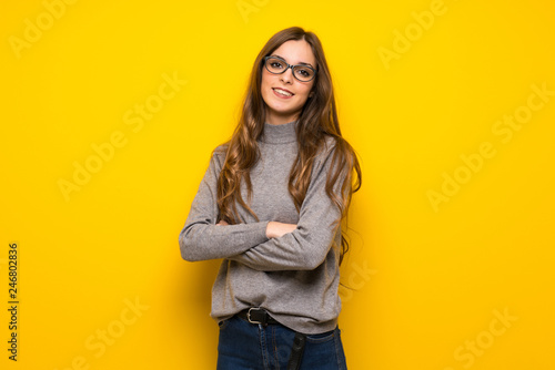 Young woman over yellow wall with glasses and happy