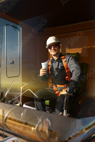 Happy engineer feel success after good work. He sit a top of crane cabin drink coffee and looking beautiful sunset