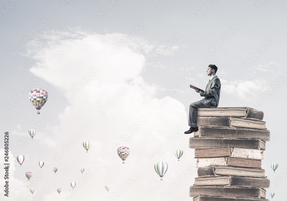Man student reading book and aerostats flying around in air Man student reading book and aerostats flying around in air