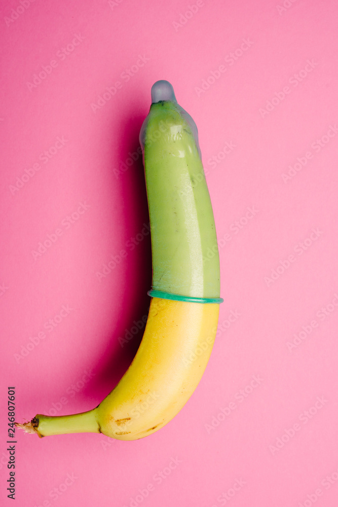 Fototapeta premium Banana with green condom in front of pink background