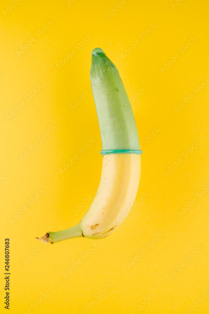 Fototapeta premium Banana with green condom in front of yellow background