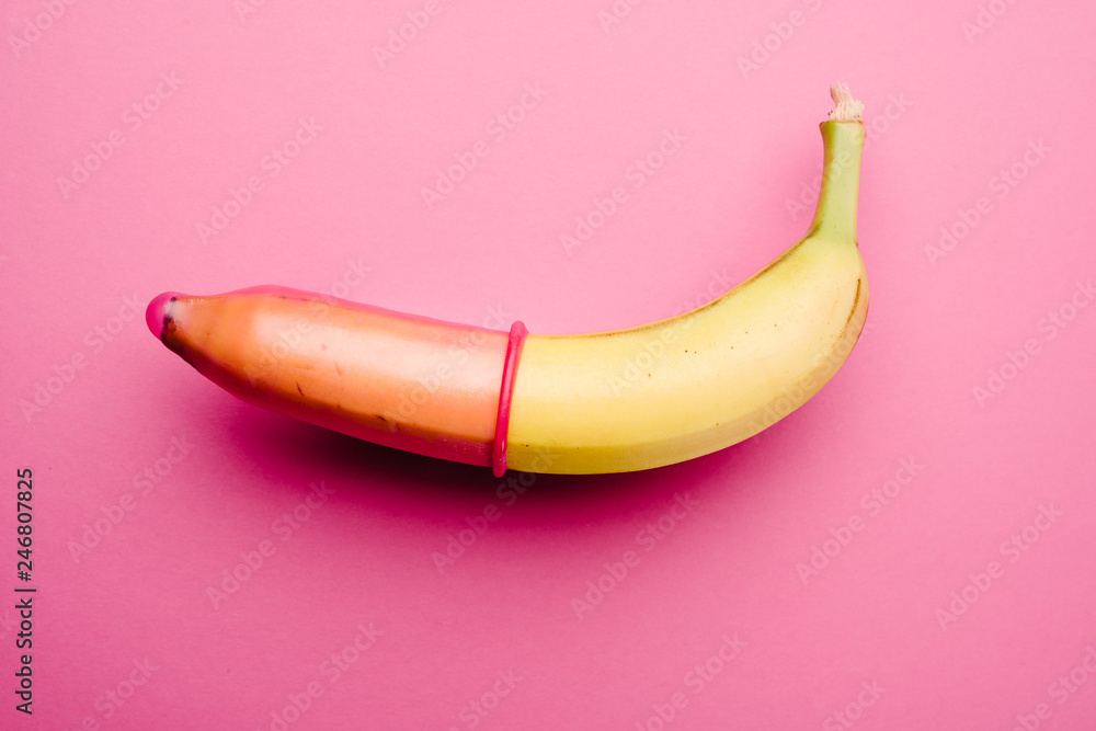 Fototapeta premium Pink condom on banana in front of pink background