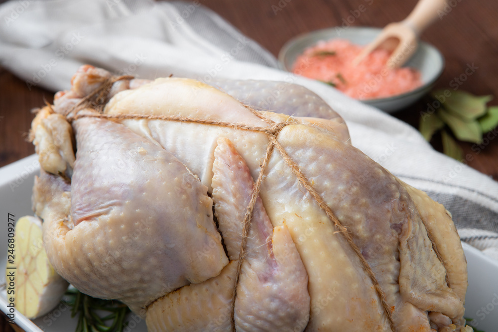 Raw guinea fowl in the white baking dish with garlic and rosemary and Himalayan pink salt next to it in a bowl Raw guinea fowl in the white baking dish with garlic and rosemary and Himalayan pink salt next to it in a bowl