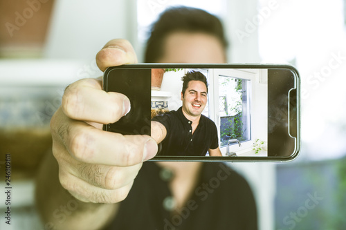 Guy making a selfi with a cell phone and smiling at home